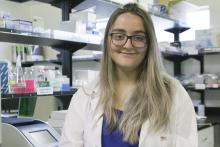 Kimberley Barrett wears a white lab coat and stands in a research lab.