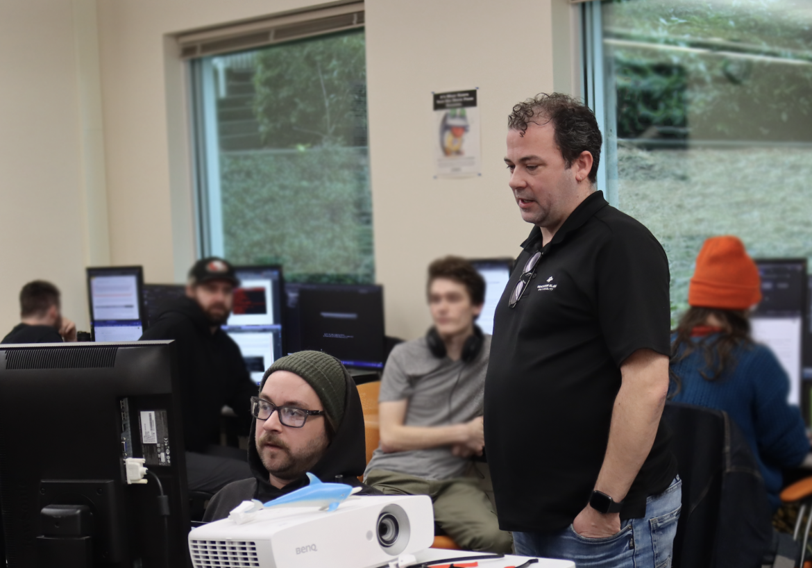 Information Technology and Applied Systems Instructor Brandon Britt observes carl belie on a project.
