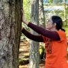 A woman wearing an orange t-shirt for Truth and Reconciliation Day putting her hands on a large tree in an act of gratitude/